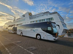 Large white luxury tour bus at a dock with water in the background and an Allied Coaches logo on the side of the vehicle